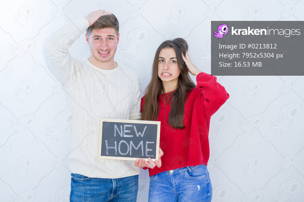 Beautiful young couple over white background holding blackboard with new home text stressed with hand on head, shocked with shame and surprise face, angry and frustrated. Fear and upset for mistake.