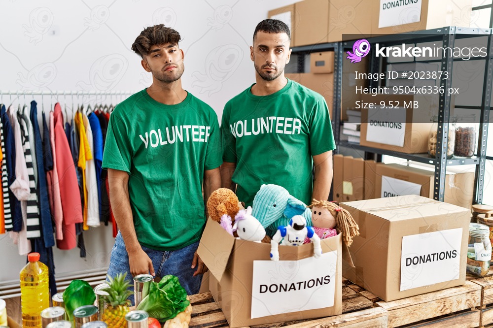 Young gay couple wearing volunteer t shirt at donations stand looking sleepy and tired, exhausted for fatigue and hangover, lazy eyes in the morning. 