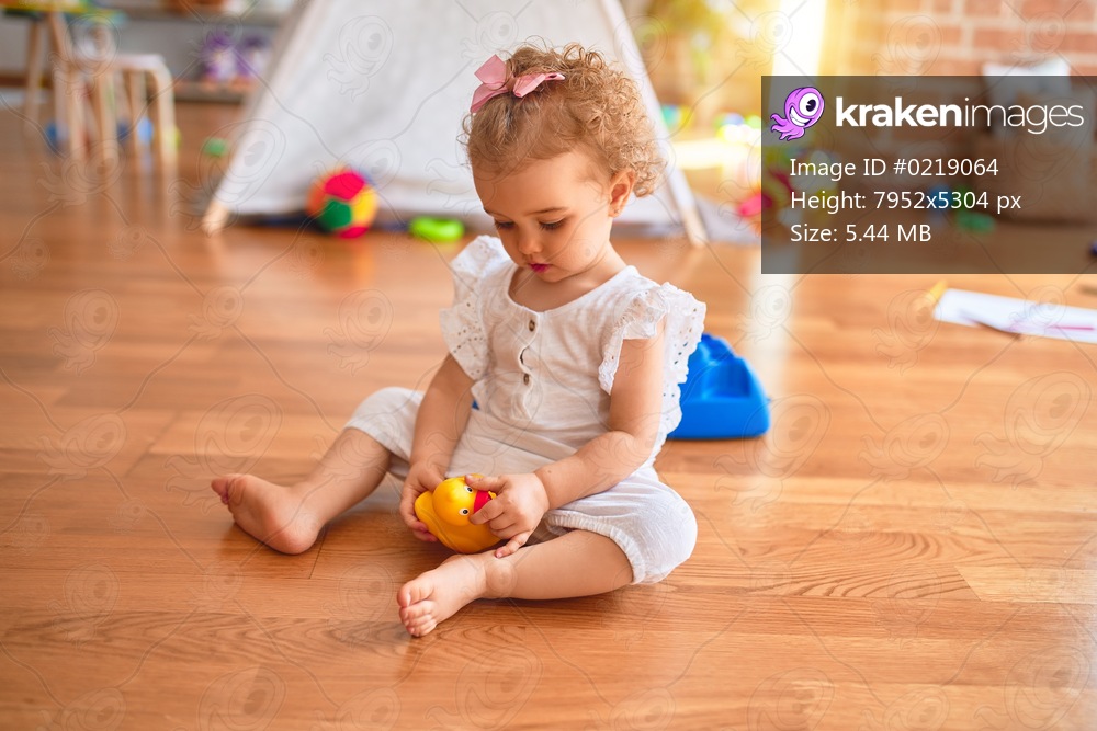 Beautiful caucasian infant playing with toys at colorful playroom. Happy and playful at kindergarten.