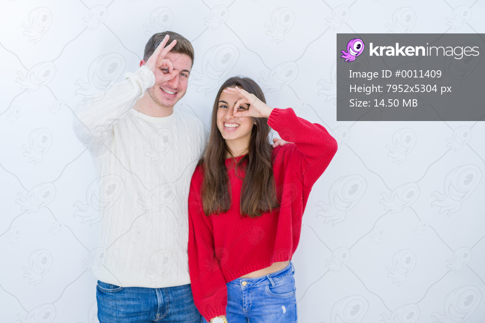 Beautiful young couple over white isolated background doing ok gesture with hand smiling, eye looking through fingers with happy face.