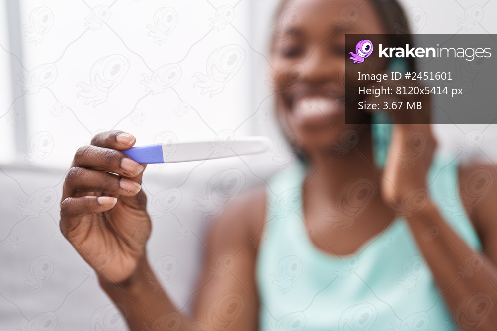 African american woman talking on smartphone holding pregnancy test at home
