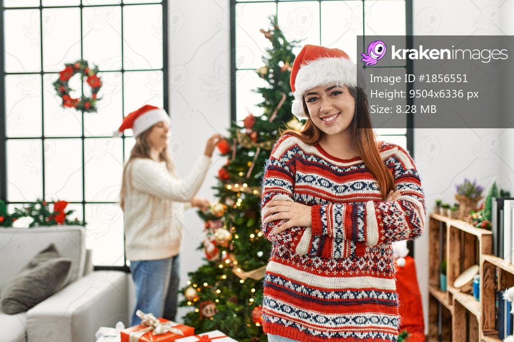 Beautiful couple at home standing by christmas tree happy face smiling with crossed arms looking at the camera. positive person. 