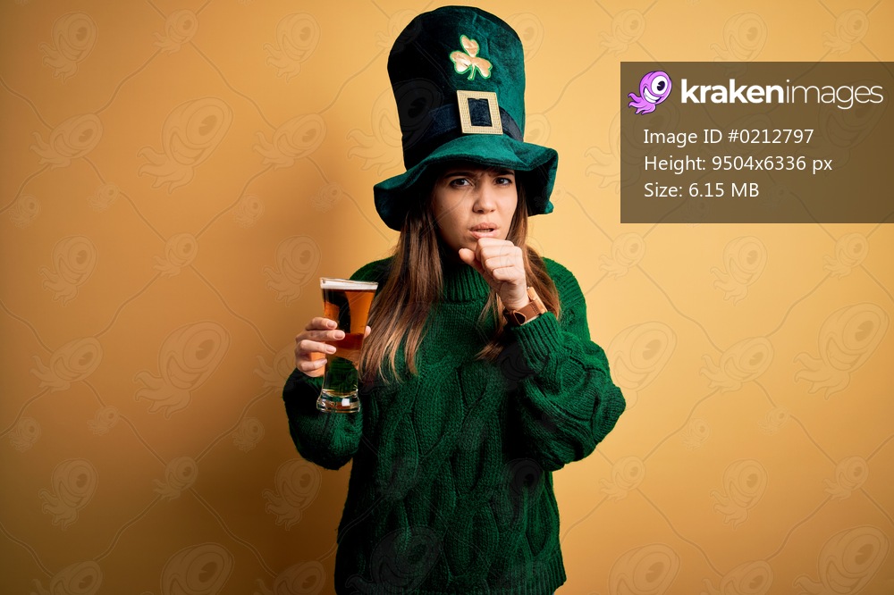 Young beautiful woman wearing green hat drinking glass of beer on saint patricks day feeling unwell and coughing as symptom for cold or bronchitis. Health care concept.