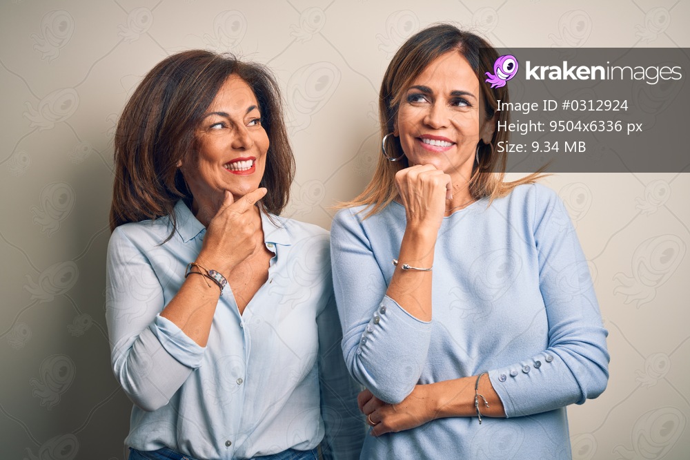 Middle age beautiful couple of sisters standing over isolated white background with hand on chin thinking about question, pensive expression. Smiling with thoughtful face. Doubt concept.