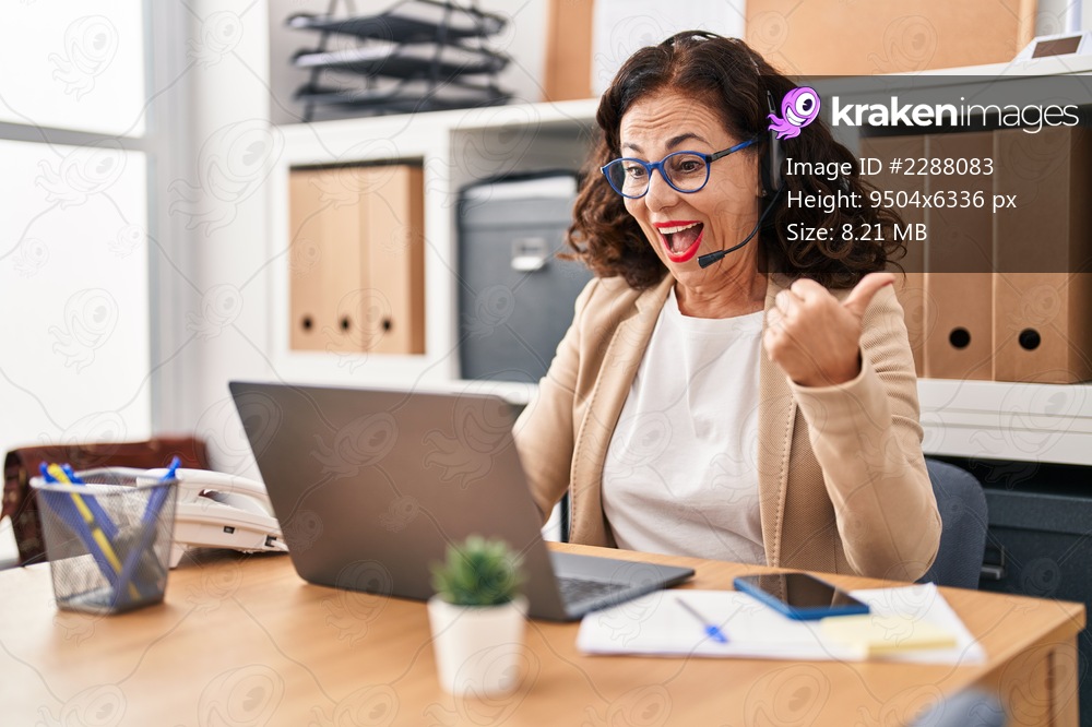 Middle age woman wearing call center agent headset pointing thumb up to the side smiling happy with open mouth 