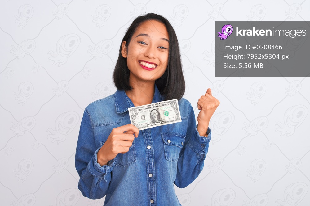 Young beautiful chinese woman holding one dollar standing over isolated white background screaming proud and celebrating victory and success very excited, cheering emotion