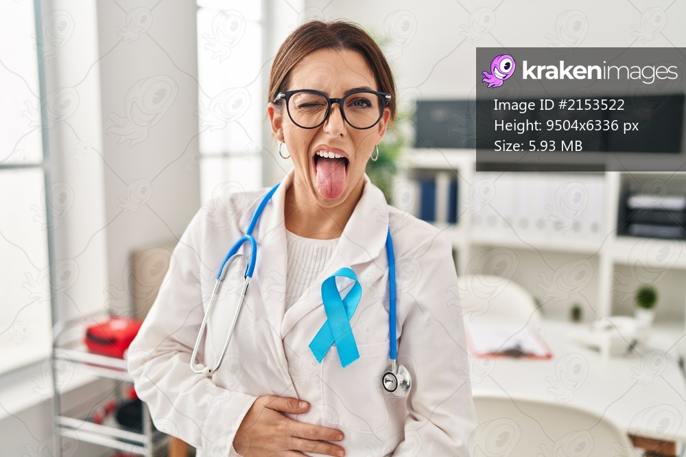 Young brunette doctor woman wearing stethoscope at the clinic sticking tongue out happy with funny expression. emotion concept. 
