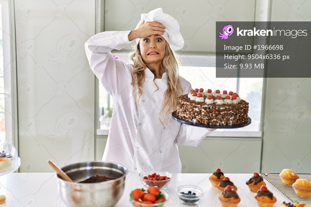 Young caucasian pastry chef woman cooking pastries and cake at the kitchen stressed and frustrated with hand on head, surprised and angry face 