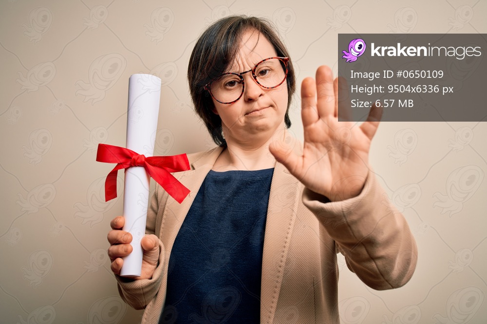 Young down syndrome business woman holding univeristy diploma award over isolated background with open hand doing stop sign with serious and confident expression, defense gesture