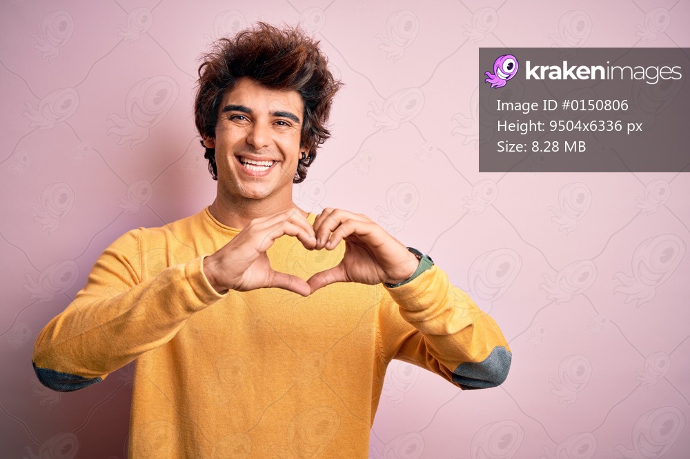 Young handsome man wearing yellow casual t-shirt standing over isolated pink background smiling in love doing heart symbol shape with hands. Romantic concept.