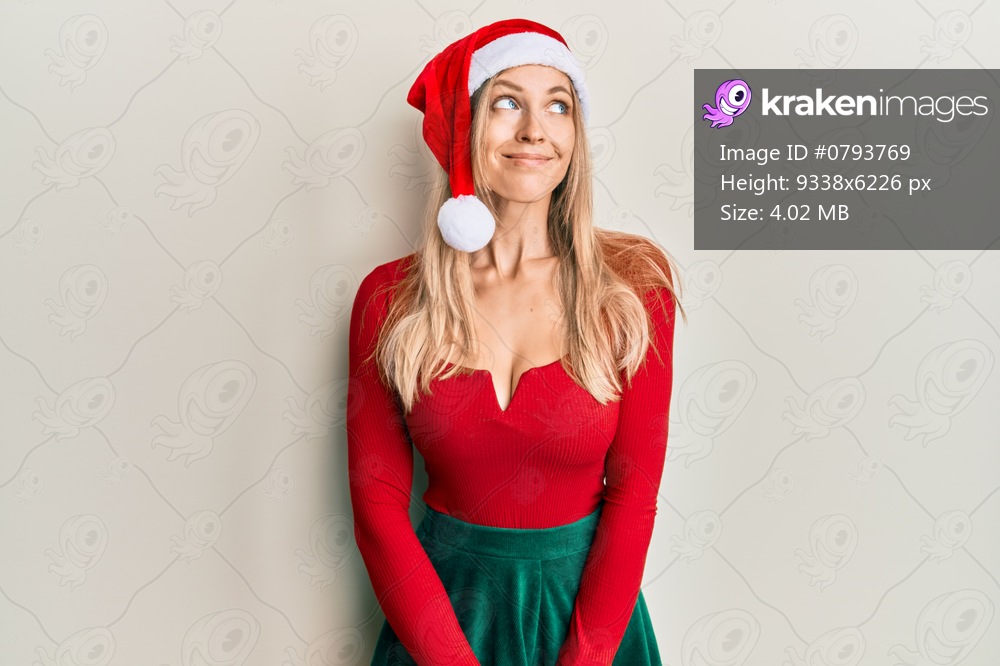 Beautiful caucasian woman wearing christmas costume and hat smiling looking to the side and staring away thinking. 