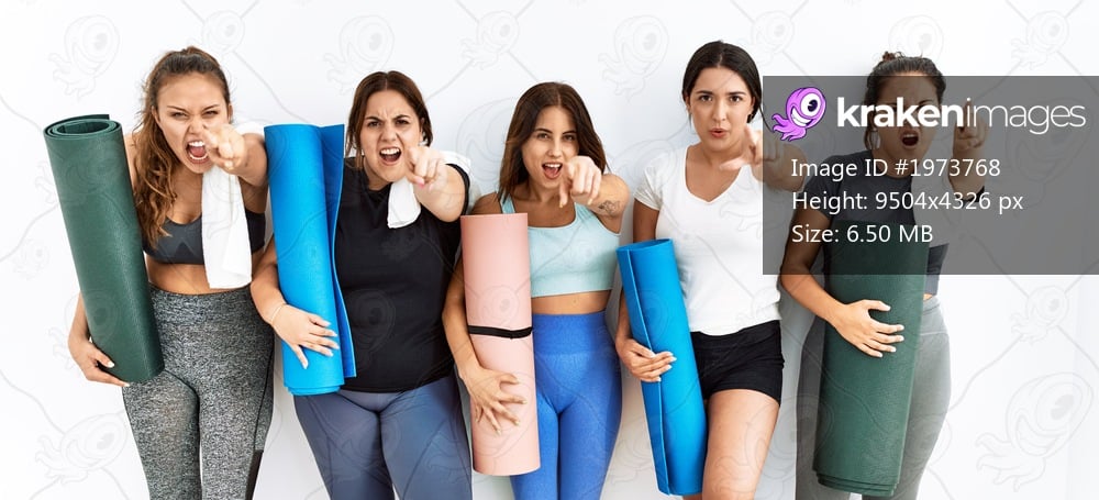 Group of women holding yoga mat standing over isolated background pointing displeased and frustrated to the camera, angry and furious with you 