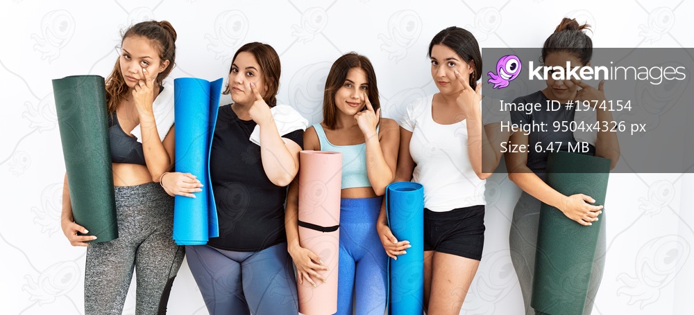 Group of women holding yoga mat standing over isolated background pointing to the eye watching you gesture, suspicious expression 
