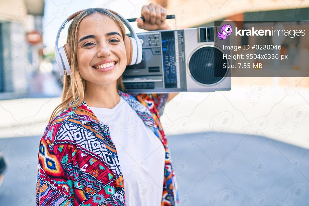 Young beautiful blonde caucasian woman smiling happy outdoors on a sunny day playing music on boombox
