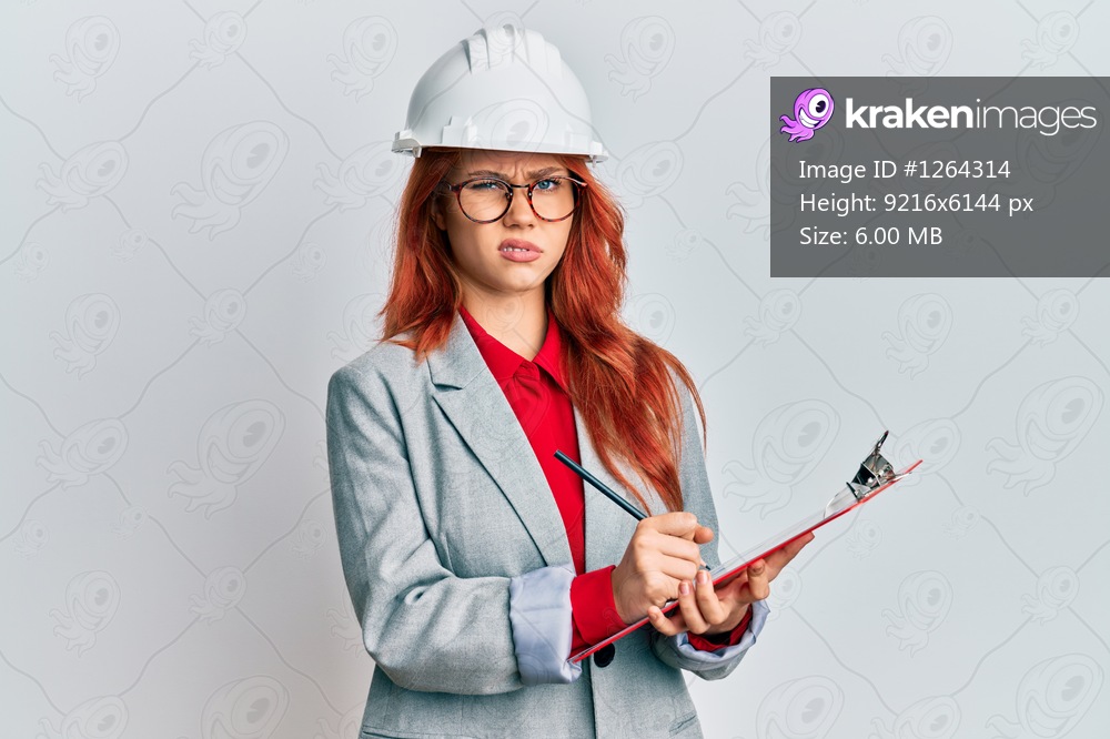 Young redhead woman wearing architect hardhat skeptic and nervous, frowning upset because of problem. negative person. 