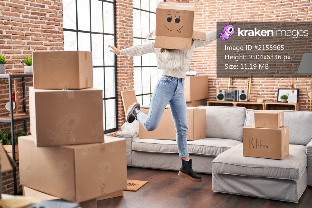 Young woman dancing with funny cardboard box on head at new home