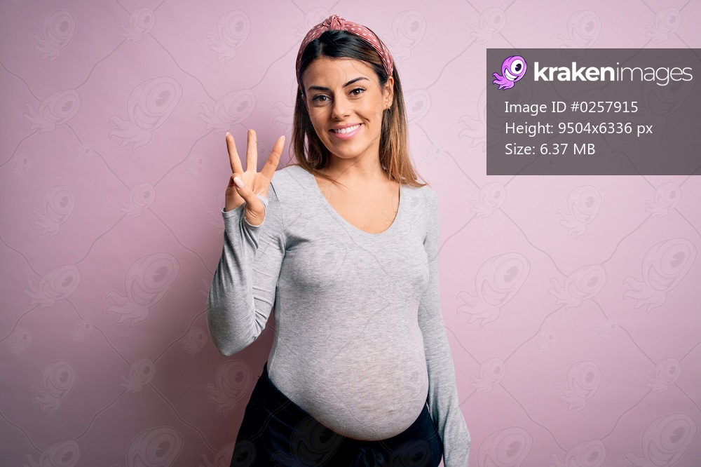 Young beautiful brunette woman pregnant expecting baby over isolated pink background showing and pointing up with fingers number three while smiling confident and happy.