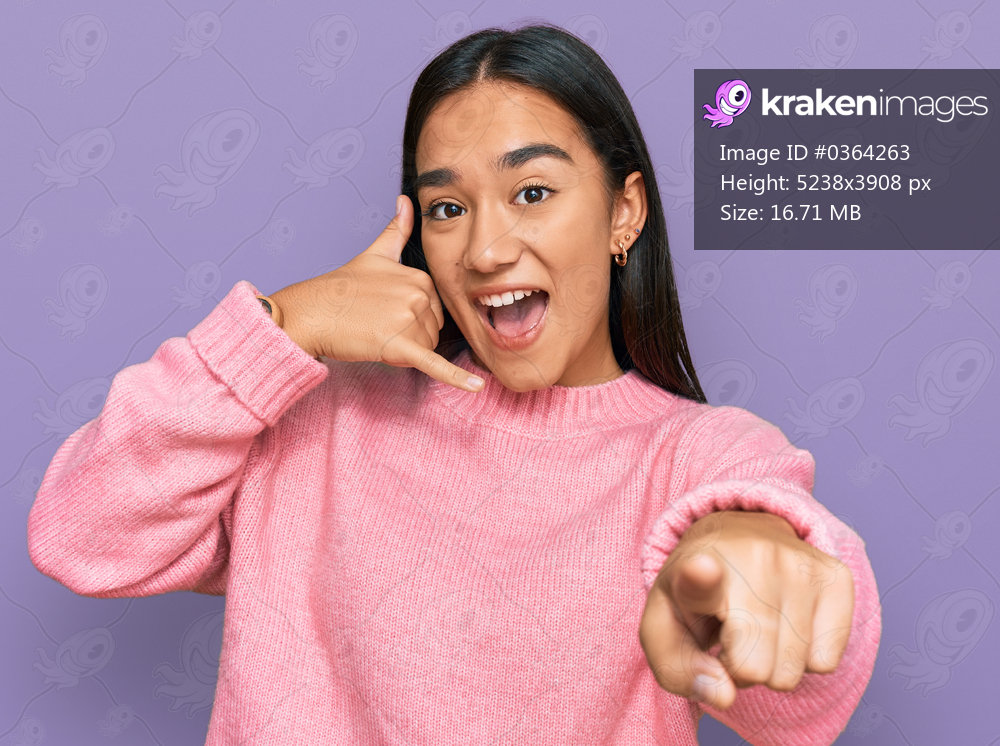 Young asian woman wearing casual winter sweater smiling doing talking on the telephone gesture and pointing to you. call me. 