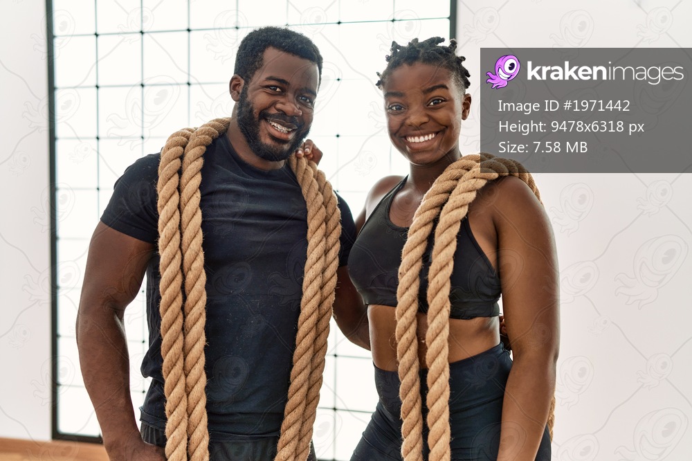 Young african american sporty couple smiling happy holding battle rope at sport center.