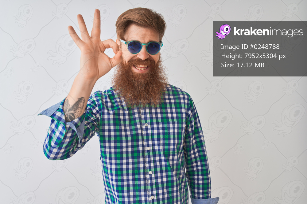 Young redhead irish man wearing casual shirt and sunglasses over isolated white background smiling positive doing ok sign with hand and fingers. Successful expression.