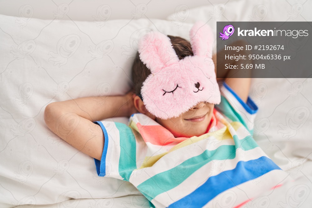 Blond child wearing sleep mask lying on bed at bedroom