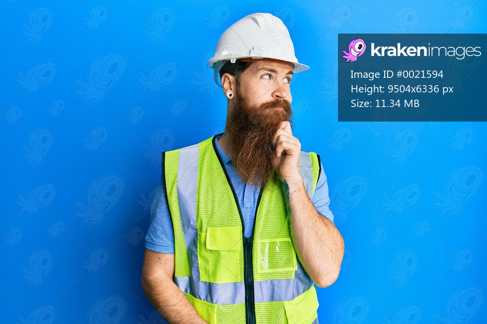 Redhead man with long beard wearing safety helmet and reflective jacket with hand on chin thinking about question, pensive expression. smiling with thoughtful face. doubt concept. 