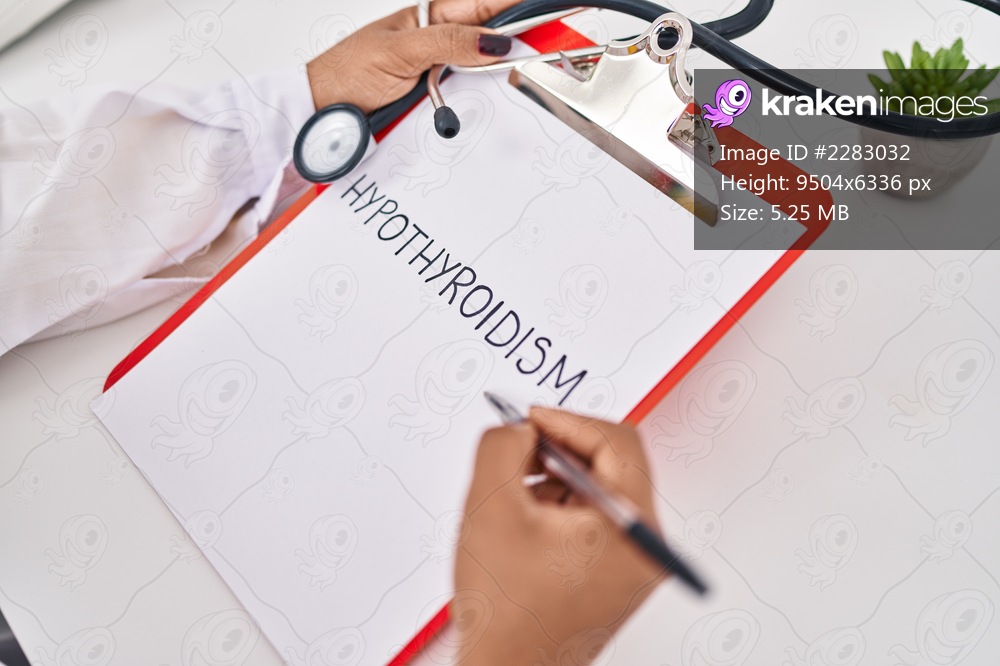 African american woman wearing doctor uniform writing hypothyroidism word on clipboard at clinic