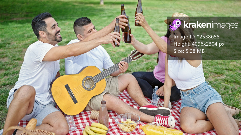 Group of people toasting with bottle of beer having picnic at park