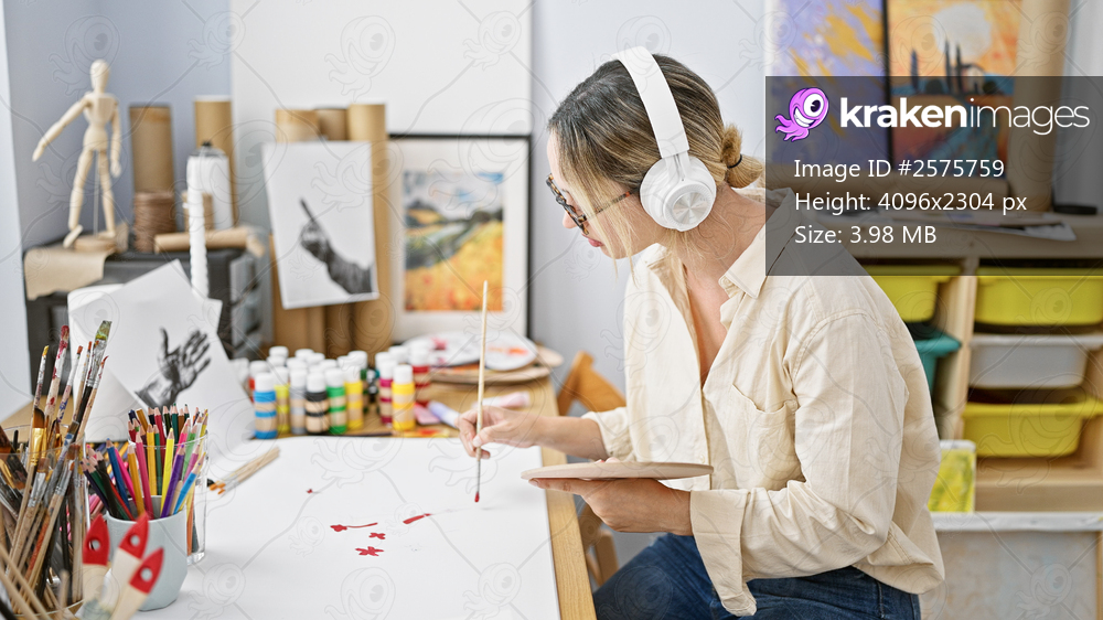 Young blonde woman artist drawing on paper listening to music at art studio