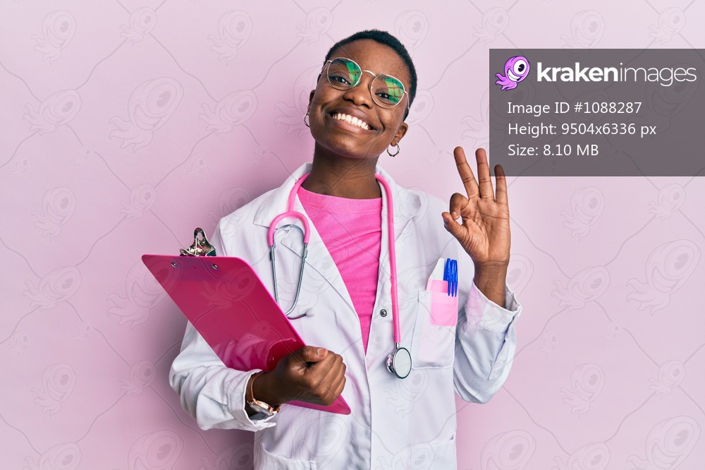 Young african american woman wearing doctor stethoscope holding clipboard doing ok sign with fingers, smiling friendly gesturing excellent symbol 