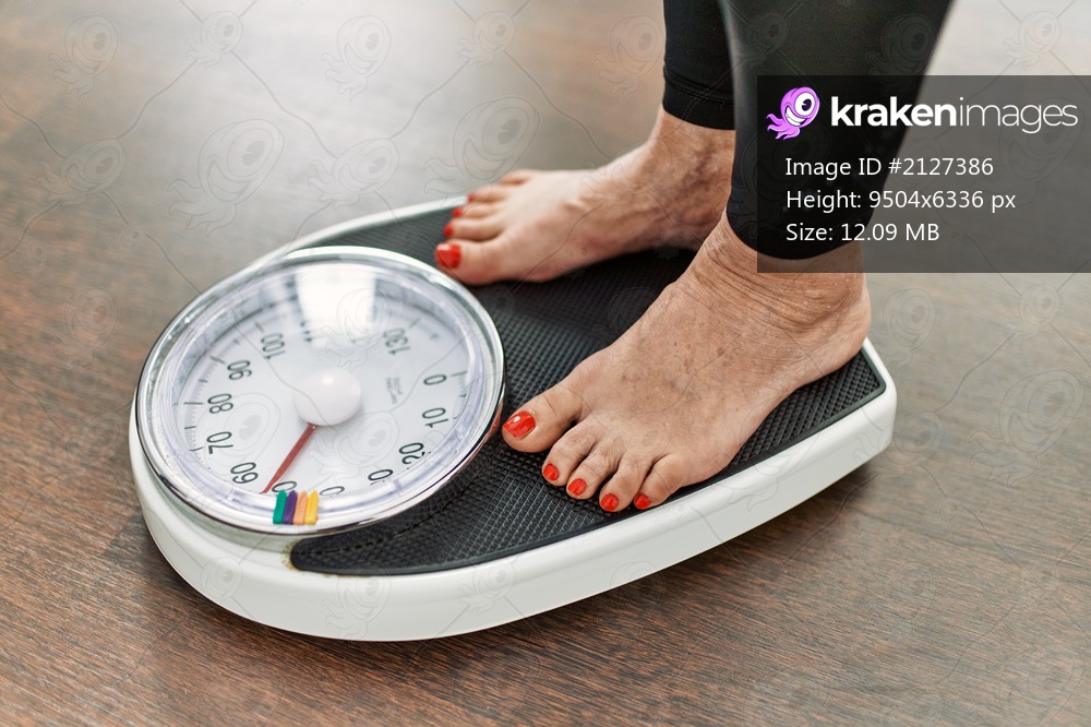 Middle age grey-haired woman using weighing machine at home