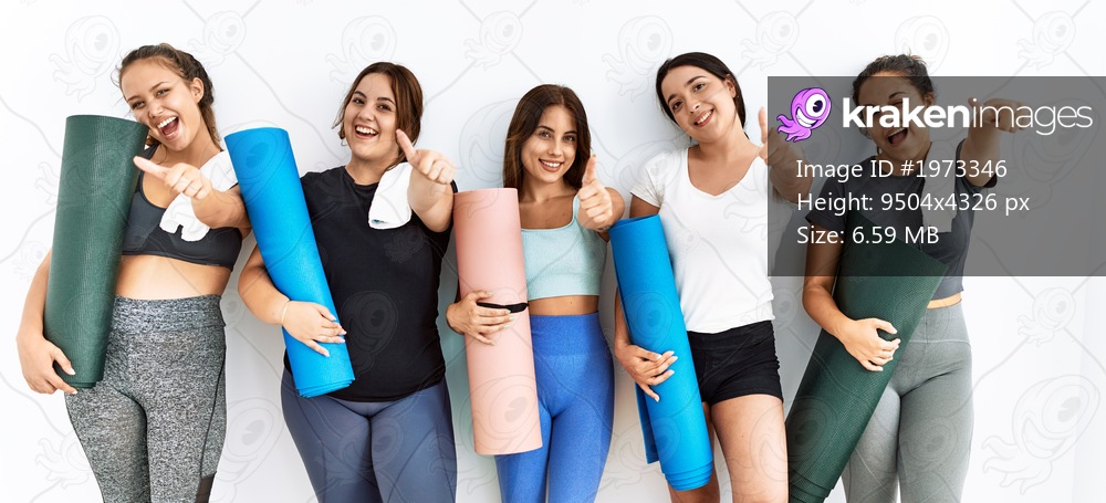 Group of women holding yoga mat standing over isolated background approving doing positive gesture with hand, thumbs up smiling and happy for success. winner gesture. 