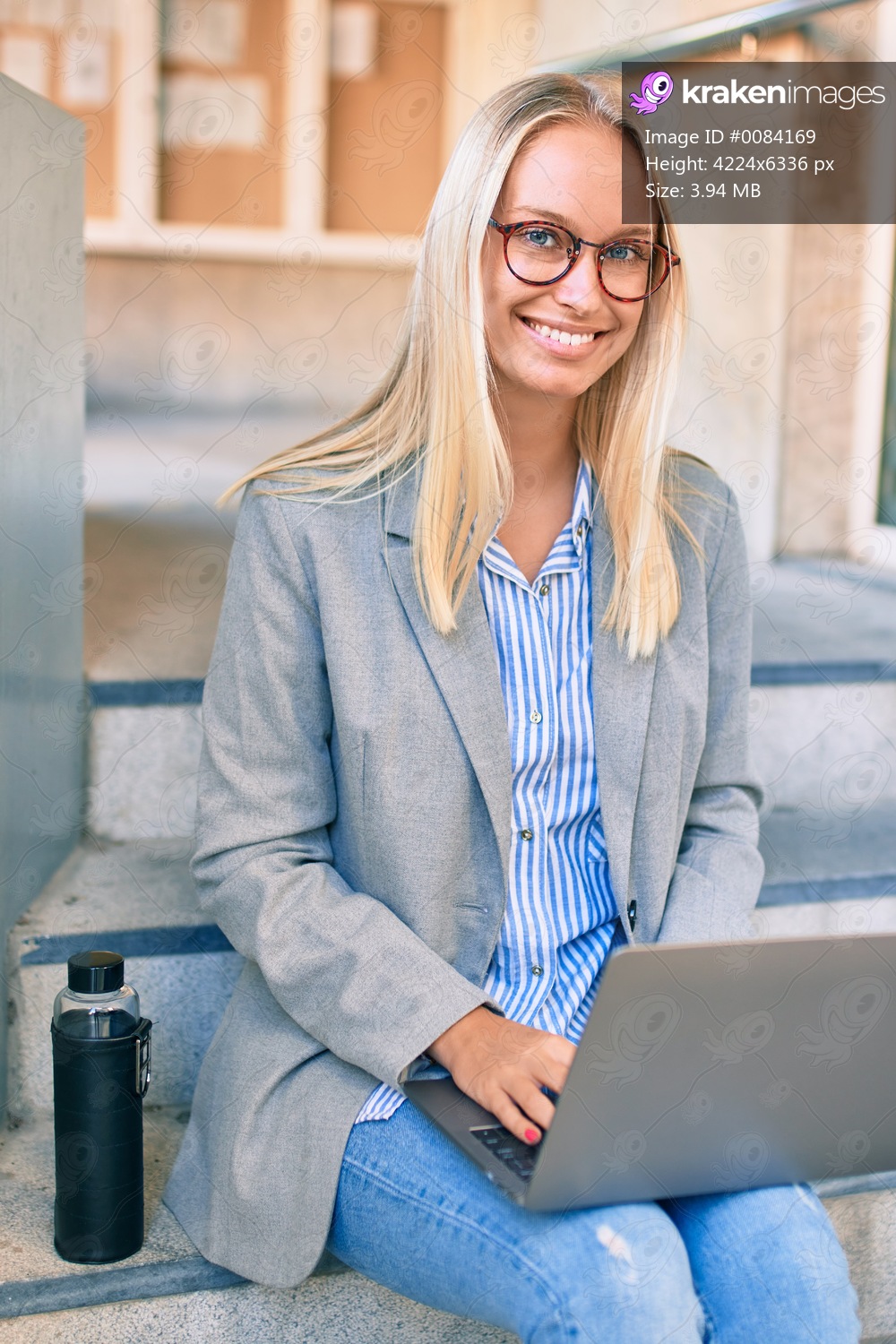 Young blonde businesswoman smiling happy working using laptop sitting on the stairs at the city.