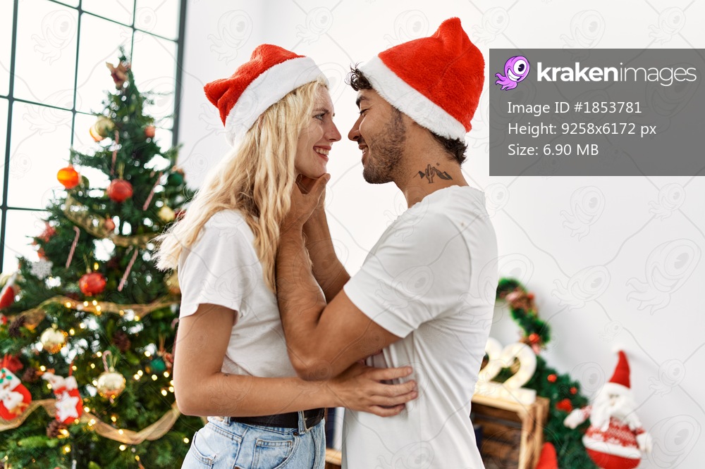 Young couple smiling happy in romantic attitude wearing christmas hat at home.