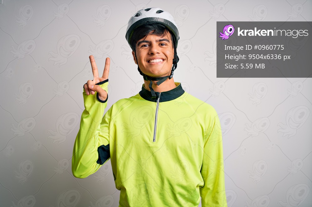 Young handsome cyclist man wearing security bike helmet over isolated white background smiling with happy face winking at the camera doing victory sign. Number two.