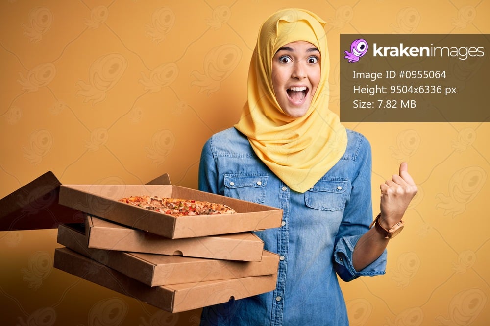 Young girl wearing muslim hijab holding boxes with Italian pizza over yellow background screaming proud and celebrating victory and success very excited, cheering emotion