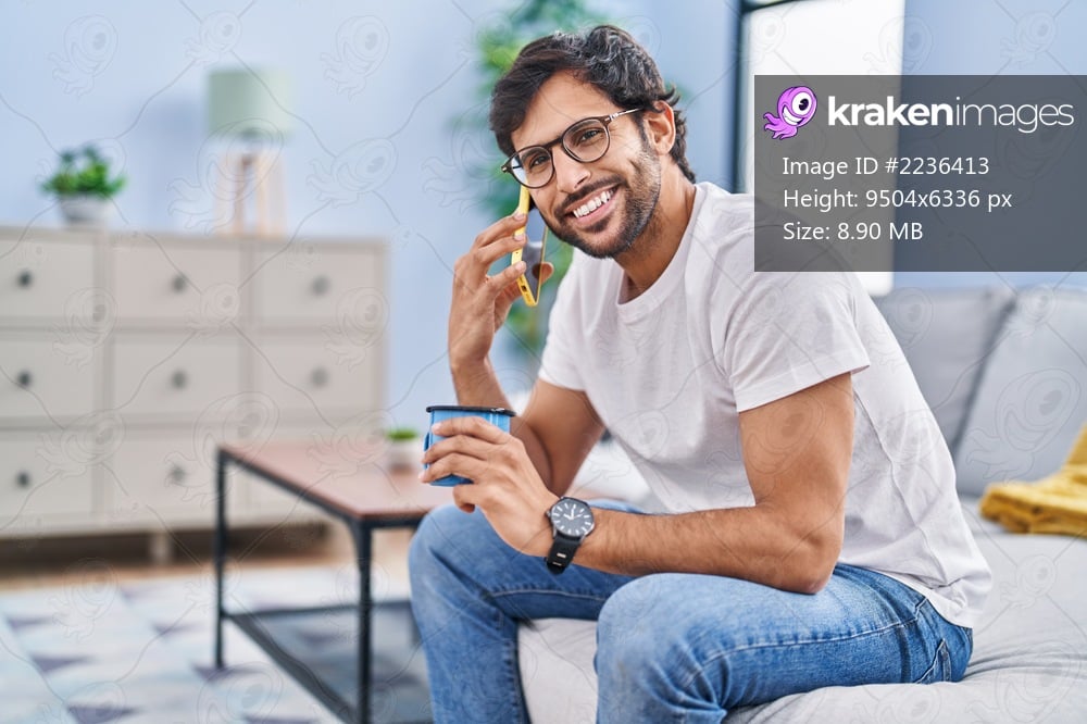 Young hispanic man drinking coffee and talking on the smartphone at home