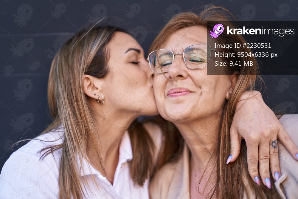 Mother and daughter smiling confident hugging each other and kissing over black background