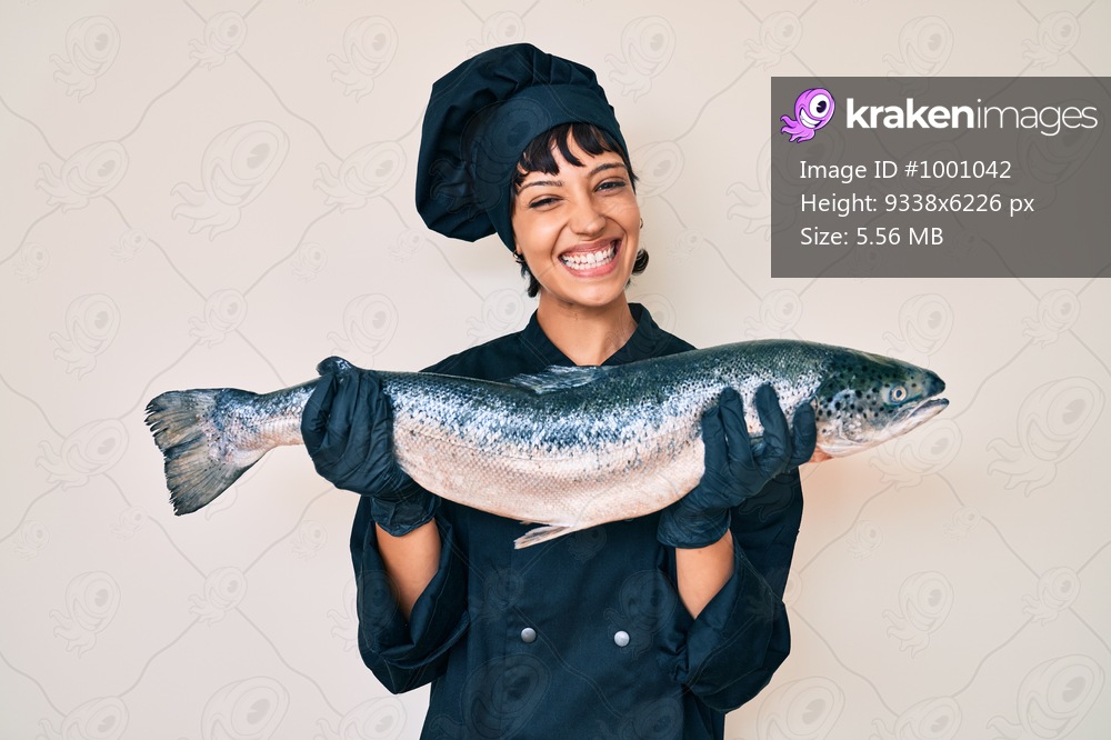 Beautiful brunettte woman professional chef holding fresh salmon fish smiling with a happy and cool smile on face. showing teeth. 