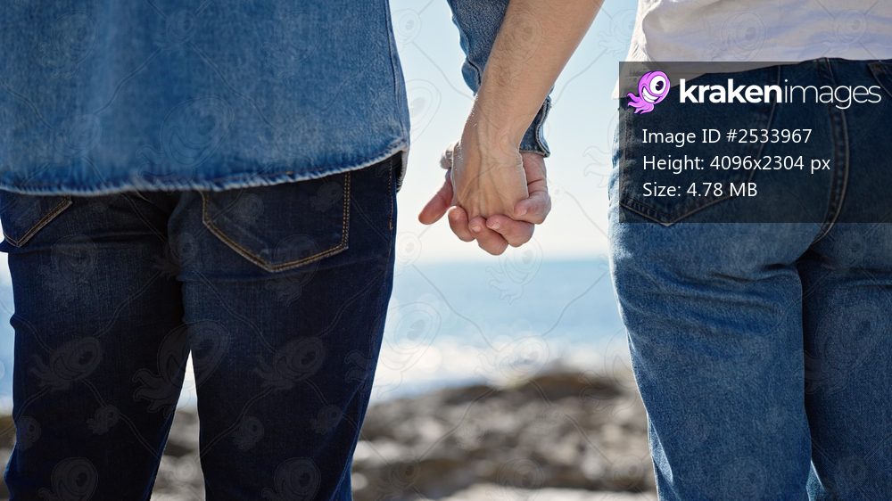 Man and woman couple standing with hands together backwards at seaside