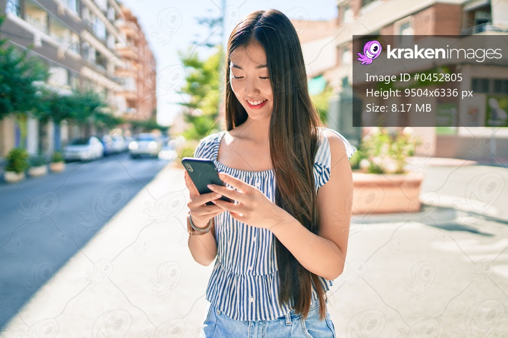 Young chinese woman smiling happy using smartphone at street of city.