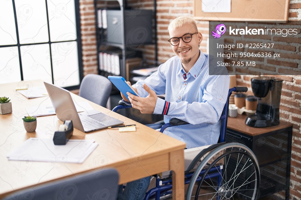 Young caucasian man business worker using touchpad sitting on wheelchair at office