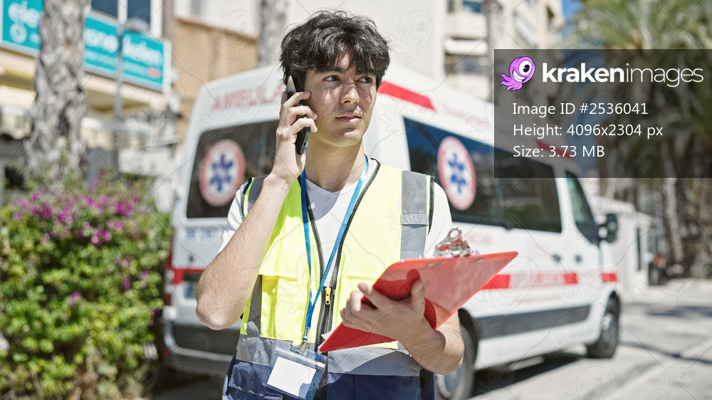 Young hispanic man nurse talking on smartphone standing by ambulance at street