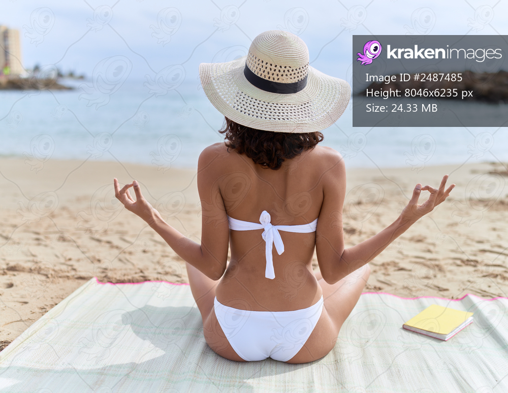 Young african american woman wearing summer hat and bikini doing yoga exercise at beach