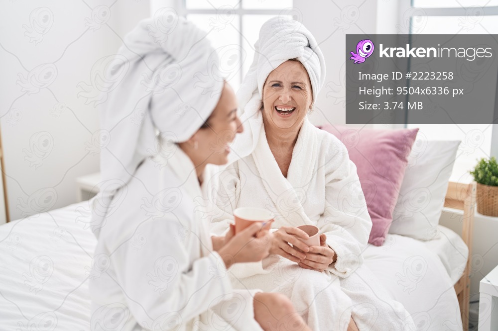 Mother and daughter wearing bathrobe drinking coffee at bedroom