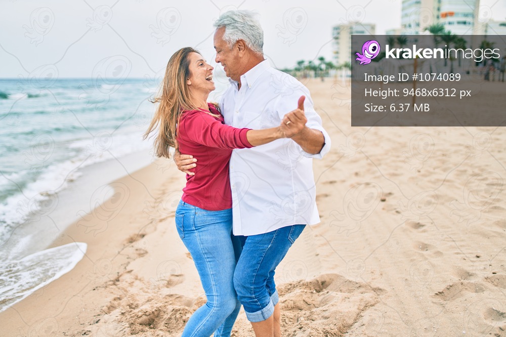 Middle age couple in love dancing at the beach happy and cheerful together