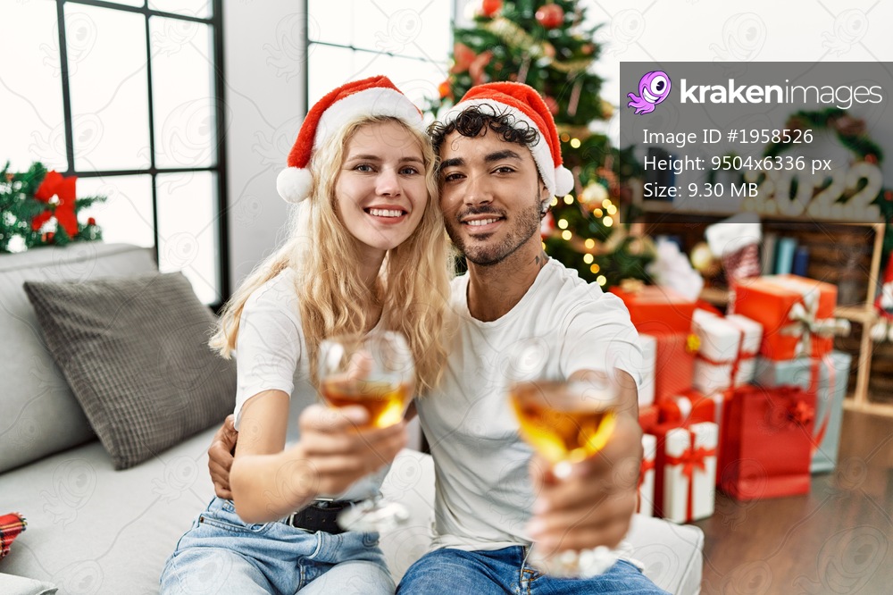 Young couple smiling happy wearing christmas hat toasting with champagne at home