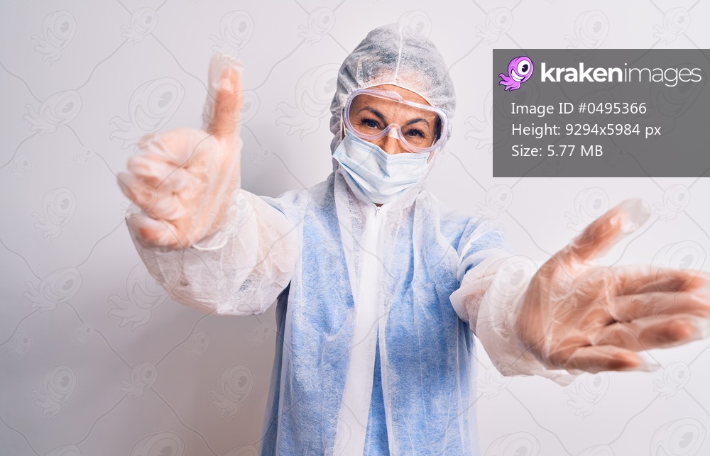 Middle age nurse woman wearing protection coronavirus equipment over white background looking at the camera smiling with open arms for hug. Cheerful expression embracing happiness.