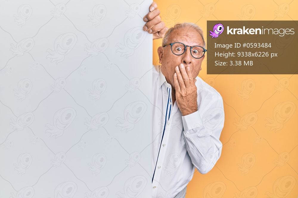 Senior caucasian man holding blank empty banner covering mouth with hand, shocked and afraid for mistake. surprised expression 