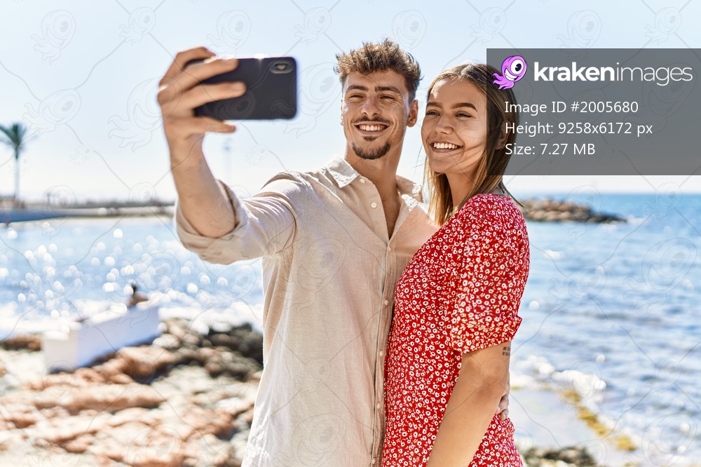 Young hispanic couple on vacation smiling happy make selfie by the smartphone at the beach